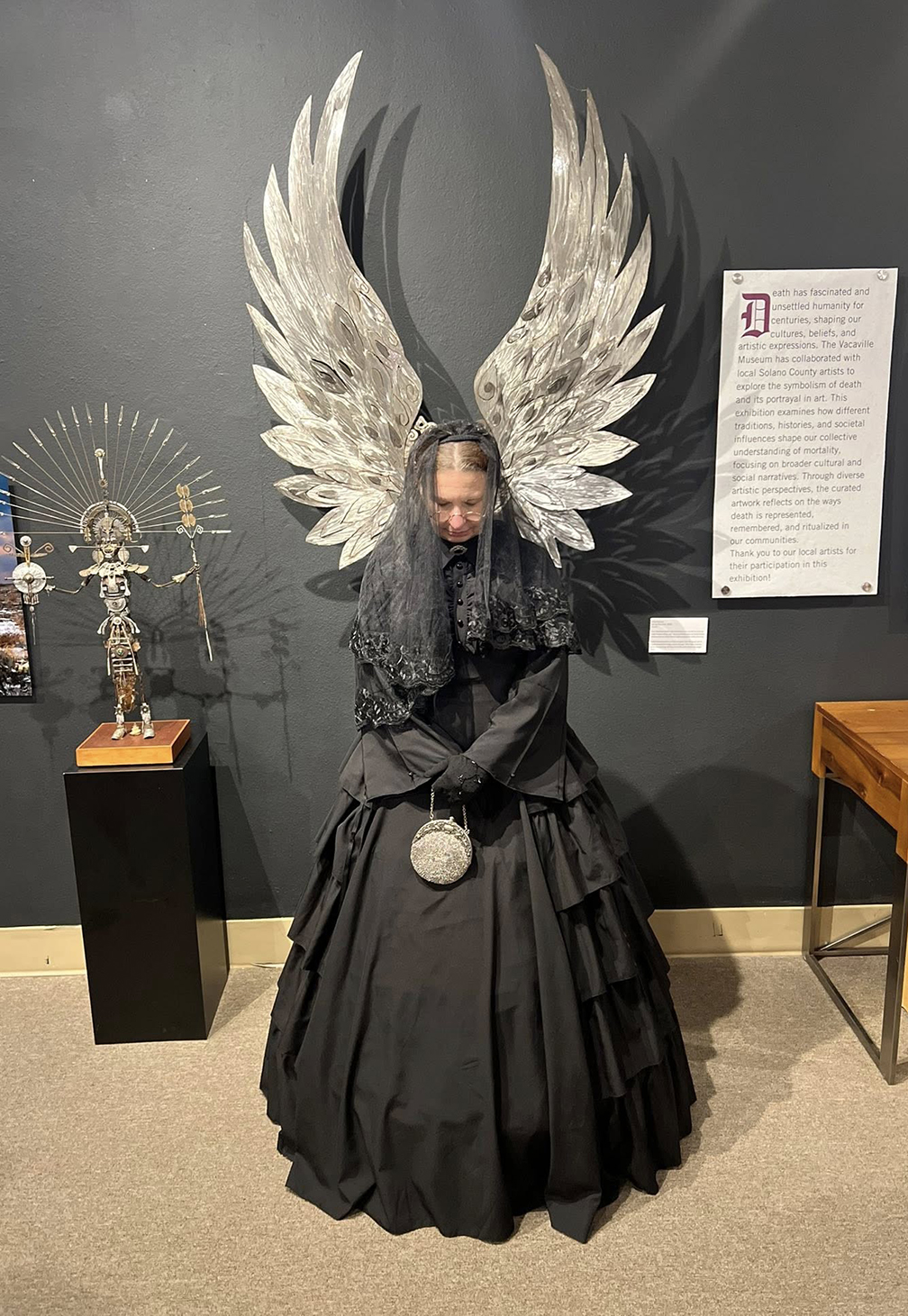 Vacaville Museum Guild member Kerri Schillinger in a mourning dress, similar in style to 1860s mourning dresses. She is pictured next to metal art by Alicia Gomez of Vallejo.