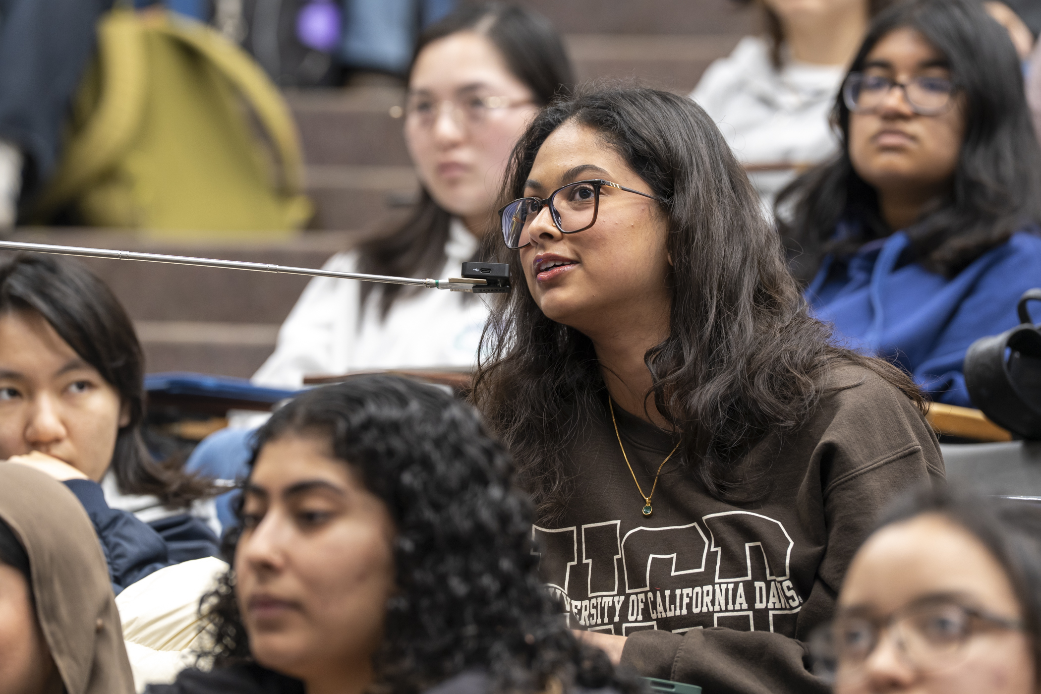 A diverse group of students listening in a lecture, with one woman asking a question.