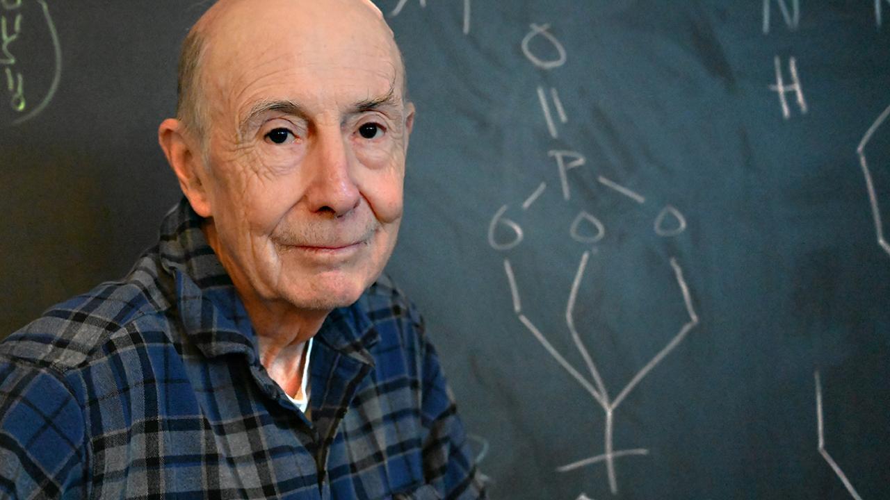 Portrait of Bruce Hammock in blue plaid shirt before a chalkboard with chemical structures